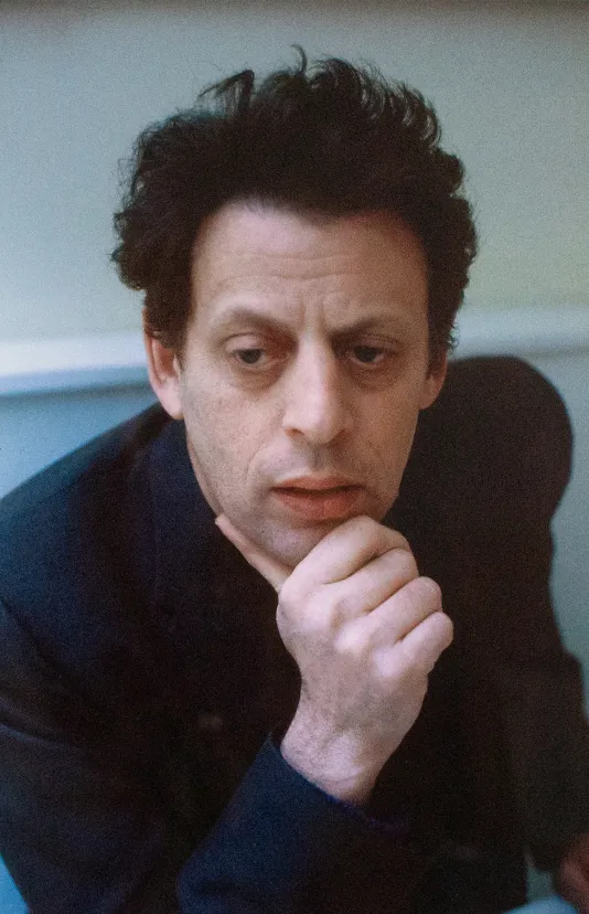 Portrait of Philip Glass reading his hand on his chin with a furrowed brow.