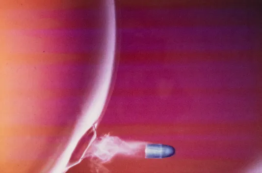 Close up shot of a silver bullet coming out of a red bubble.