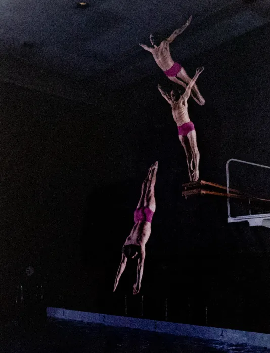 Triple exposure photograph of a man in pink shorts diving off a diving board.