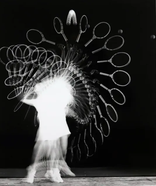 Long exposure photograph of a person hitting their tennis ball with their racket. The racket, ball, and player are in motion.