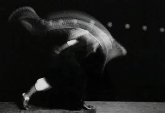 Long exposure photograph of a person throwing a pitch. The motion of their arm and the ball is blurred.