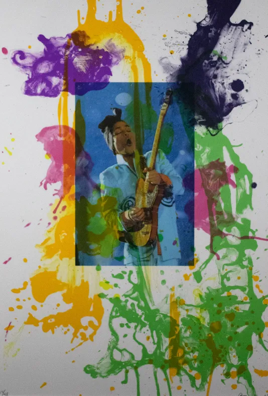 Photograph of a woman playing the guitar placed in the center of a canvas with green, purple, yellow, and pink ink splattered around it.