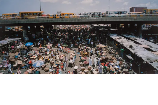 Photograph from above of a crowded street market below a bridge full of traffic.