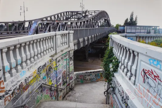 Photograph og a bridge with a staircase leading down to from it covered in colorful grafiti.