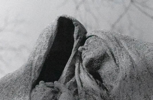 Photograph of a statue of a person wearing a scarf on their head embracing a figure to their right who has a scarf nut no face.