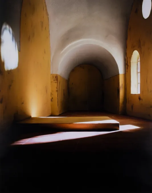 Photograph of an abandoned room with yellow walls and contrast from the shadows and natural light coming from a window on the right