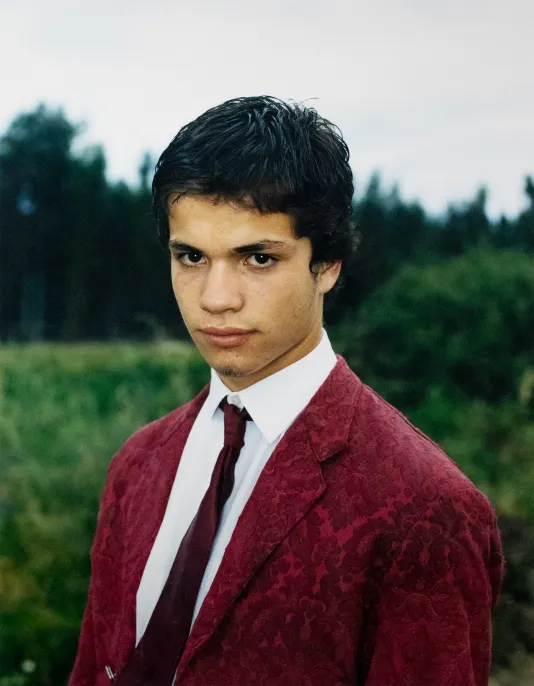 Portrait of a boy wearing a red blazer and tie looking down at the camera.