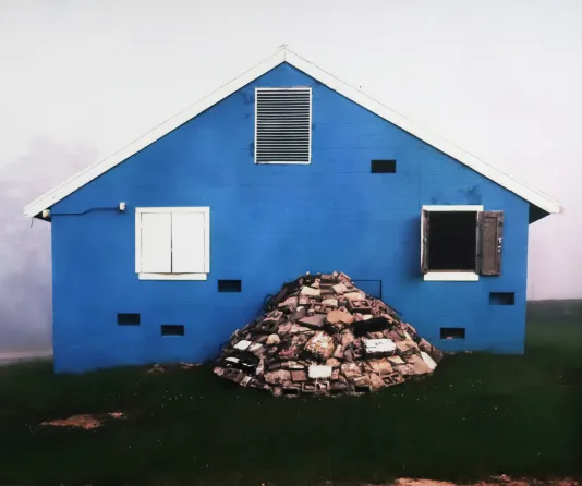Blue house surround dby fog with three windows and a pile of rubble out front.