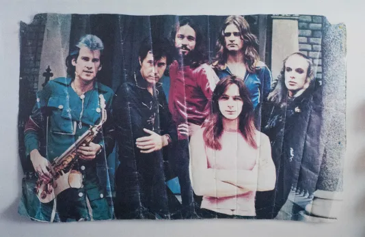 Crumpled photograph of a six person band, the man on the far left holds a saxophone.