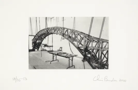Black and white photograph of a model bridge suspended in a studio.