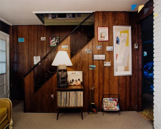 Photograph of a wood paneled basement with a shelf that has records and 70s decorations.