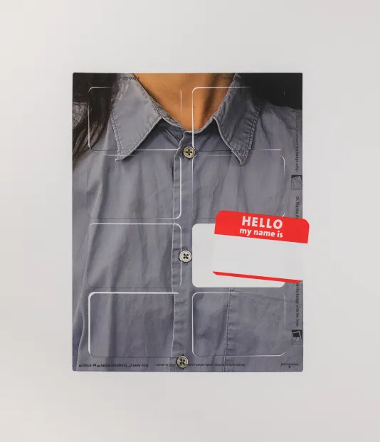 Closeup photograph of someone wearing a blue dress blouse with a "Hello, my name is" sticker on their chest.