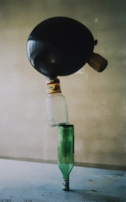 Photograph of two bottles balancing on one another with a balloon on top.