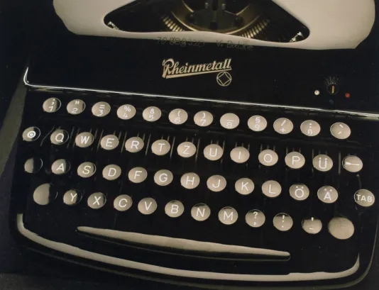 Close up photograph of a black typewriter is pictured with gray keys, carriage and a trademark logo that reads Rheinmetall
