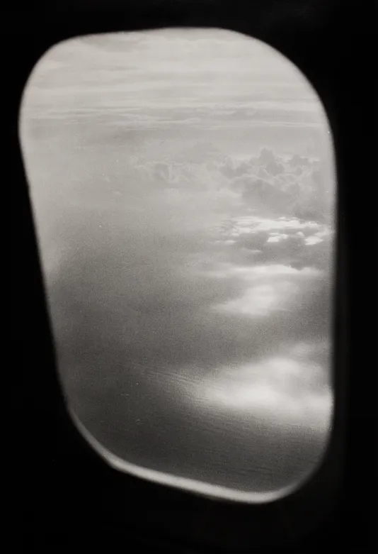 Black and white photograph of clouds outside of an airplane window.