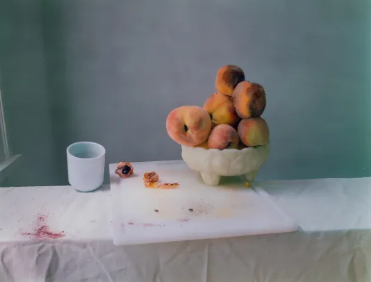 White tablecloth with a large cutting board and a bowl overflowing with peaches on top.