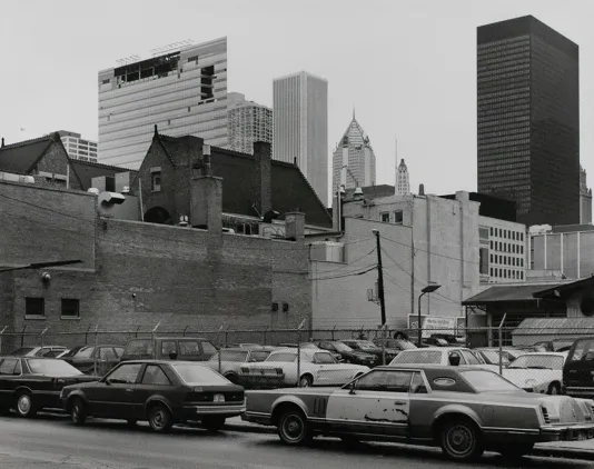 Black and white photograph of a city street with old cars parked on the side of the road.
