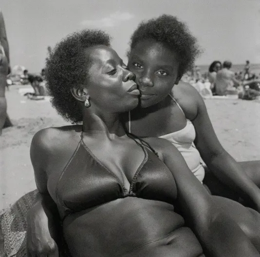 Black photograph of a mother and daughter on the beach touching cheeks.