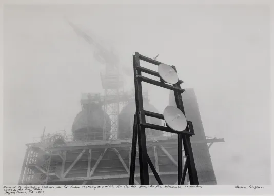 Black and white photograph of a metal structure and two satellites on a misty day.