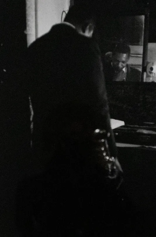 Black and white image of a man with his back o the camera and his face reflected on a camera in front of him.
