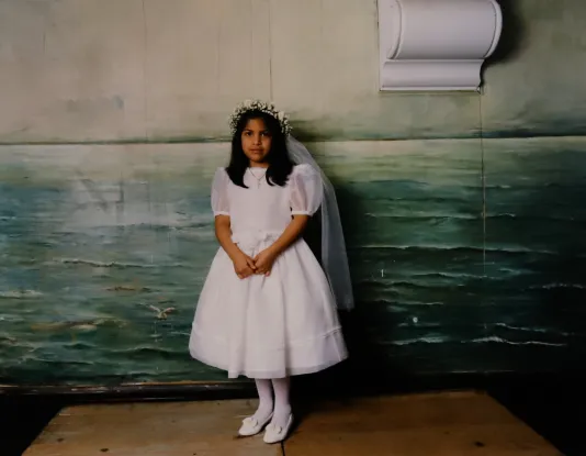 A young girl in a white communion gown poses for her. photo with her hands together.