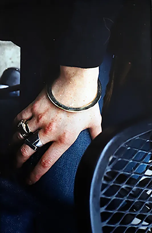 Photograph of a hand with two rings and a treacle resting on the person's thigh under a black metal table.