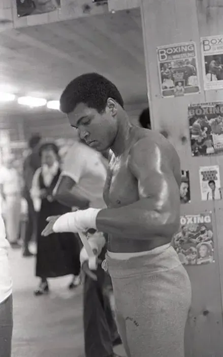 Blake and white photograph of Mohamad Ali wrapping his left hand in tape in preparation for a fight.