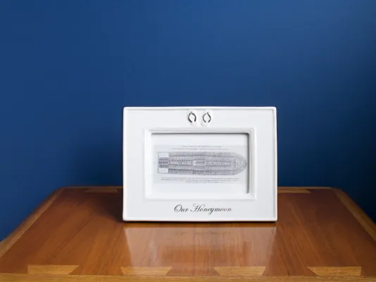 Photograph of a small framed sketch on a wooden table with a blue wall behind it.