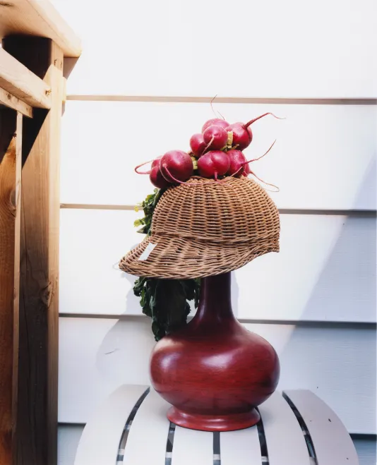 The base of a lamp with a hat on top and radishes on top of the hat meant to look like a person's profile