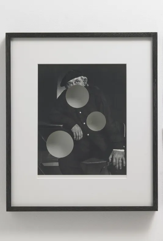 Black and white portrait of a man sitting with three opaque circles on his lower face, stomach, and right thigh.