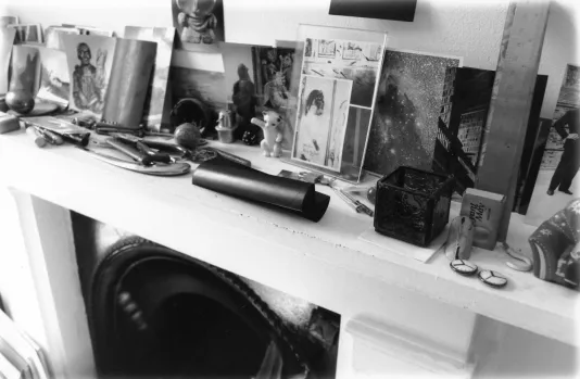 Black and white photograph of a mantle with photographs and trinkets on top.