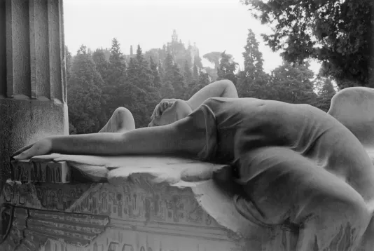 Black and white photograph of a woman lying on the edge of a balcony looking at the sky with trees in the background.