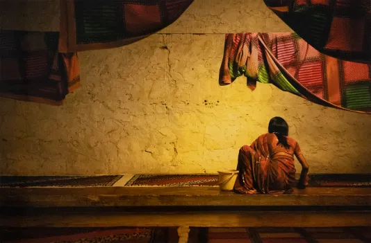 Image of a woman in India cleaning part of the building framed by hanging laundry.