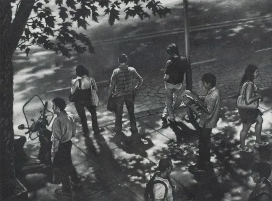 Overhead shot of a group of 7 people on a sidewalk waiting for the bus.