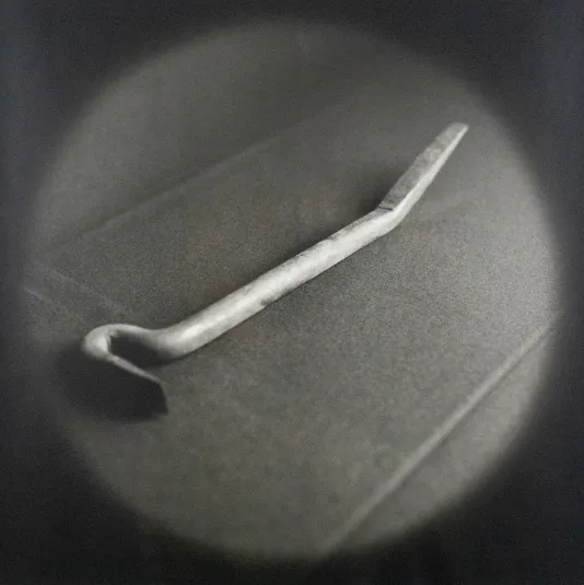 Black and white image of a bent crow bar lit with a circular spotlight.