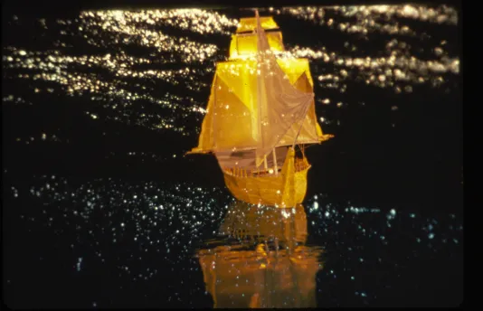 Golden illuminated sailboat cruising through what appears to be a sparkly dark sea.