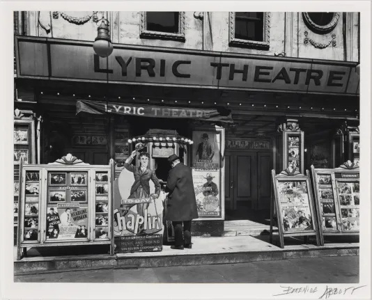 Black and white photograph of a theatre with a man in a suite standing at the front ticket booth.