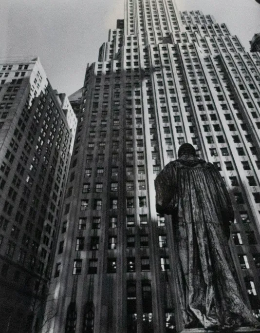 Black and white photograph of a statue from behind with a tall skyscraper in the background.