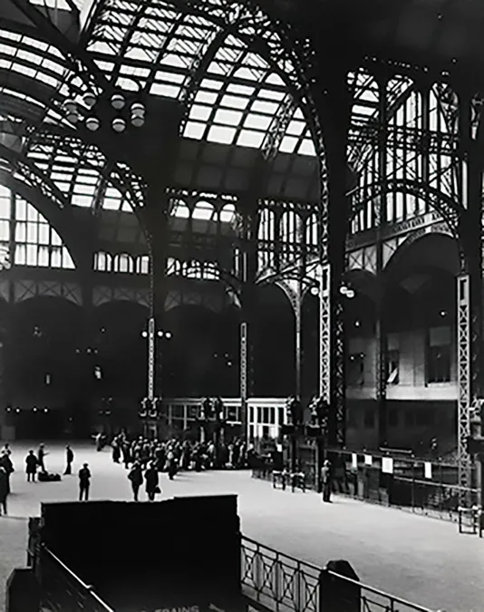 Black and white photograph of a train station with high ceilings made of window panels.