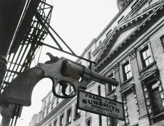 Large sign for a gunsmith featuring a huge pistol on the side of the building.