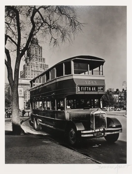 Black and white photograph of an old school double decker bus with New York City buildings in the background.