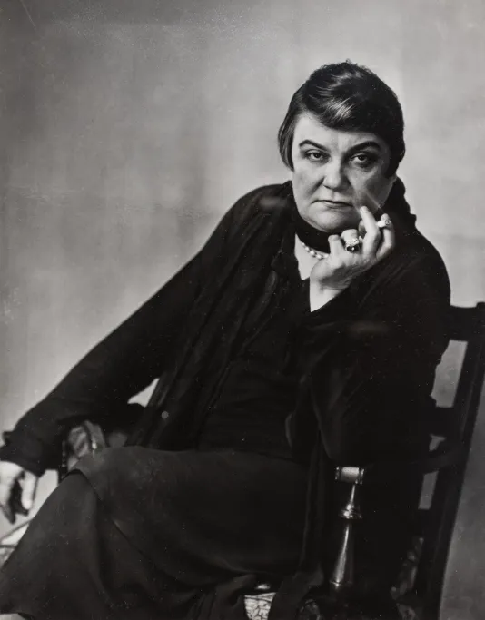 Black and white photograph of a dragqueen sitting in a chair smoking a cigarette.