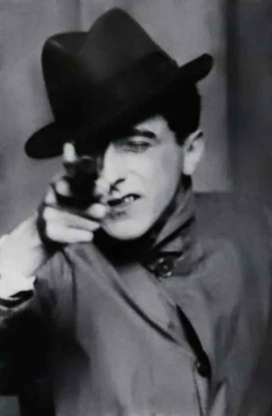 Black and white image of a man in a top hat pointing a gun towards the camera.